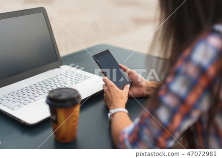 Attractive young woman reading a text message on her cell phone. Girl sitting outdoors using 47072981