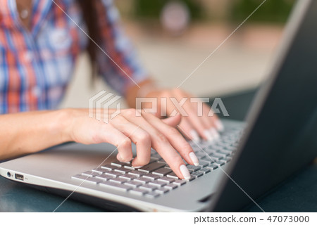 Young woman typing on a laptop keyboard working outdoors 47073000
