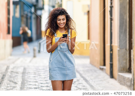 North African woman walking on the street looking at her smart p 47073258