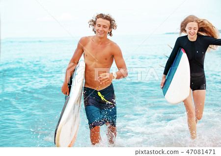 Surfers at the beach- Smiling couple of surfers walking on the beach and having fun in summer 47081471