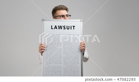 young man keeps in front of him a poster with the inscription lawsuit isolated on a light background young man keeps in front of him a poster with the inscription lawsuit isolated on a light background 47082293
