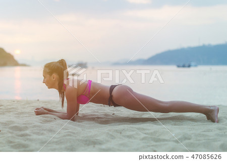 Young woman in swimsuit exercising on beach stretching her legs during sunset at sea. Fitness girl Young woman in swimsuit exercising on beach stretching her legs during sunset at sea. Fitness girl 47085626