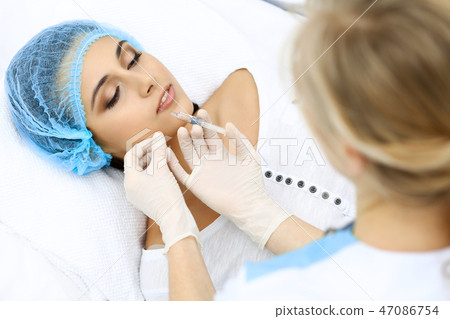 Professional cosmetologist making injection in face, lips. Young woman gets syringe with filler for Professional cosmetologist making injection in face, lips. Young woman gets syringe with filler for 47086754