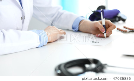 Female doctor filling up prescription form while sitting at the desk in hospital closeup. Healthcar Female doctor filling up prescription form while sitting at the desk in hospital closeup. Healthcar 47086886