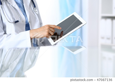 Woman doctor using tablet computer while sitting. Reflecting glass table is a working place of Woman doctor using tablet computer while sitting. Reflecting glass table is a working place of 47087136
