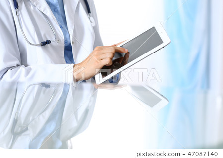 Woman doctor using tablet computer while sitting. Reflecting glass table is a working place of 47087140