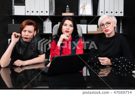 Three female colleagues sitting in office at table with laptop 47089754