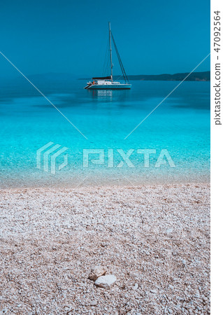 Pebble beach and white catamaran yacht boat in calm azure blue lagoon water at anchor 47092564