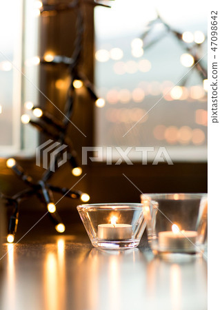 candles burning on window sill with garland lights 47098642