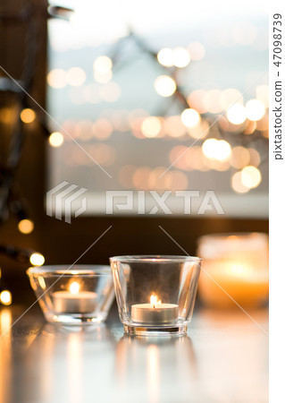 candles burning on window sill with garland lights 47098739
