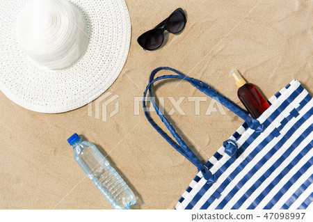 beach bag, sunscreen, sunglasses and hat on sand 47098997