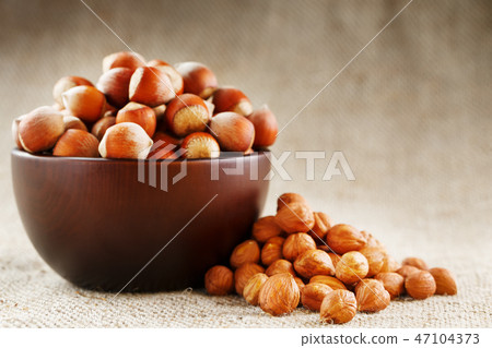 Peeled hazelnuts in a wooden, dark brown cup Peeled hazelnuts in a wooden, dark brown cup 47104373