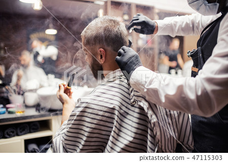 Hipster man client visiting haidresser and hairstylist in barber shop, smoking a pipe. Hipster man client visiting haidresser and hairstylist in barber shop, smoking a pipe. 47115303