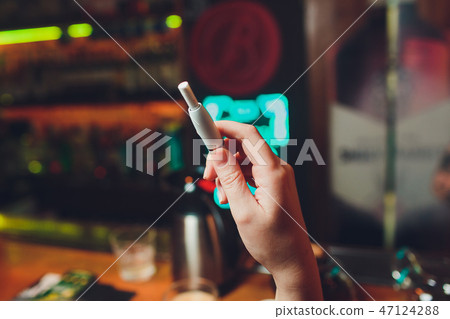 IQOS heat-not-burn tobacco product technology. Woman holding e-cigarette in his hand before smoking. IQOS heat-not-burn tobacco product technology. Woman holding e-cigarette in his hand before smoking. 47124288