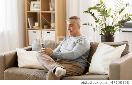 man with smartphone sitting on sofa at home 47130168