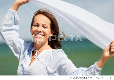 happy woman with shawl waving in wind on beach 47130224
