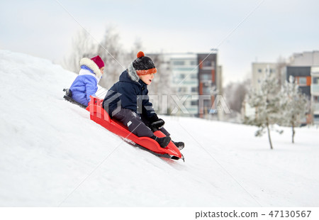 kids sliding on sleds down snow hill in winter 47130567