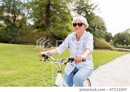 happy senior woman riding bicycle at summer park happy senior woman riding bicycle at summer park 47131047
