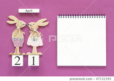 Calendar April 21 and pair of wooden easter bunnies, white notepad on purple paper background 47132393