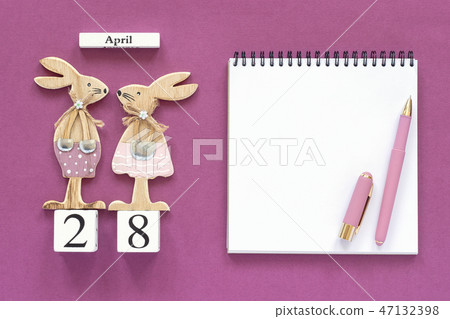 Calendar April 28, pair wooden easter bunnies, white notepad on purple paper background. Concept 47132398