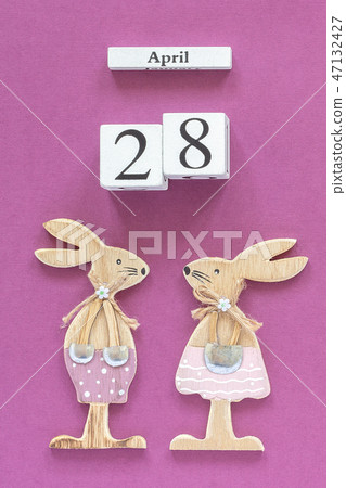 Wooden cubes calendar April 28 and pair of wooden easter bunnies on purple paper background. Concept 47132427
