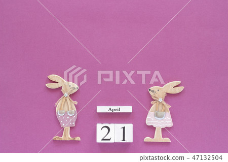 Wooden cubes calendar April 21 and pair of wooden easter bunnies on purple paper background. Concept 47132504