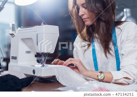 Cropped image of female tailor stitching fine lace with sewing machine sitting in dressmaking studio 47134251