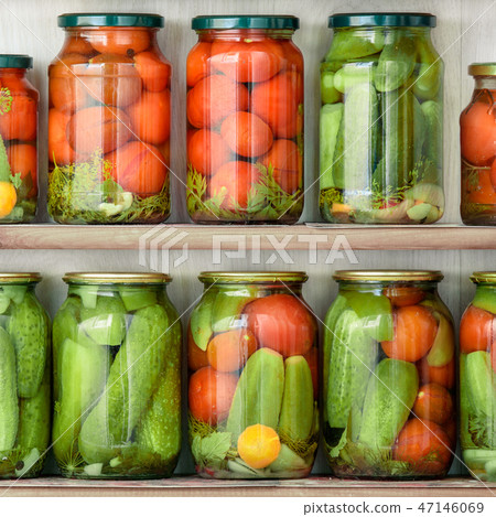 Glass jars close up with home canned vegetables standing in rows on wooden shelves. 47146069