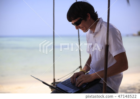 Traveler man relaxing on swing at beautiful landscape white sand beach using laptop, Businessman on Traveler man relaxing on swing at beautiful landscape white sand beach using laptop, Businessman on 47148522