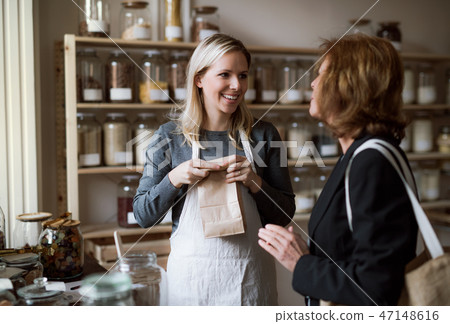 A female shop assistant serving a senior customer in a zero-waste shop. A female shop assistant serving a senior customer in a zero-waste shop. 47148616