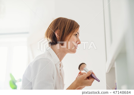 A young woman putting on a make-up in the morning in a bathroom. A young woman putting on a make-up in the morning in a bathroom. 47148684