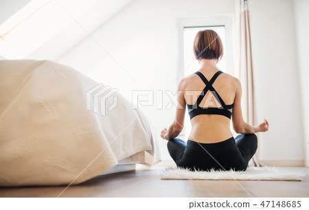 Rear view of young woman doing yoga exercise indoors in a bedroom. Copy space. Rear view of young woman doing yoga exercise indoors in a bedroom. Copy space. 47148685