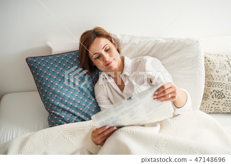 A young woman reading newspapers in bed in the morning in a bedroom. A young woman reading newspapers in bed in the morning in a bedroom. 47148696