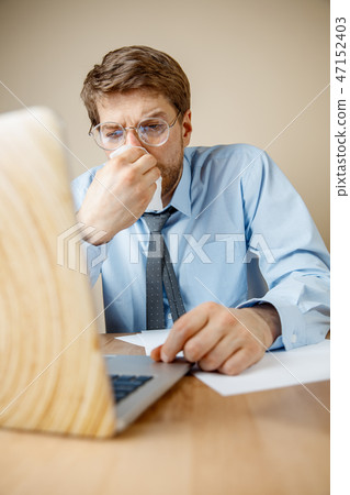 Sick man while working in office, businessman caught cold, seasonal flu. Sick man while working in office, businessman caught cold, seasonal flu. 47152403