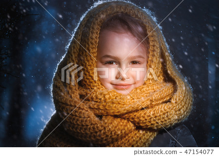 Portrait of a little charming girl in a yellow wool scarf standing outside during a snow blizzard Portrait of a little charming girl in a yellow wool scarf standing outside during a snow blizzard 47154077