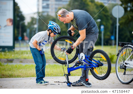 Cute little boy with his father repairing bicycle outdoors Cute little boy with his father repairing bicycle outdoors 47158447