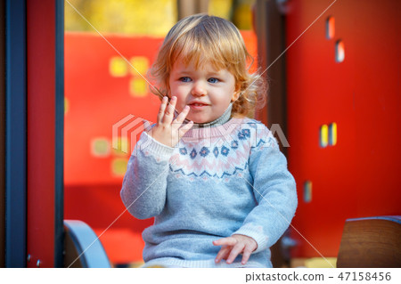 Sweet blond little baby girl in beautiful knitted dress plays outdoors at playground Sweet blond little baby girl in beautiful knitted dress plays outdoors at playground 47158456