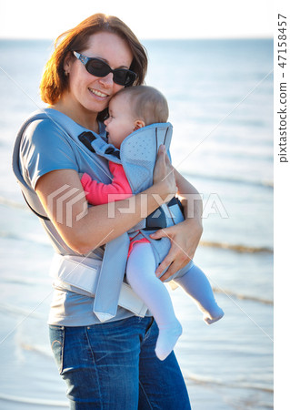Baby and mother on sea at summer day. Child in a carrier backpack 47158457