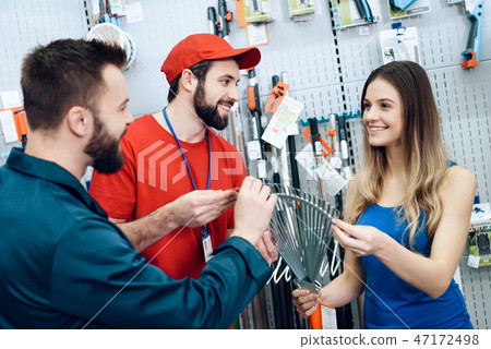 Two salesmen are showing female client new rake Two salesmen are showing female client new rake 47172498