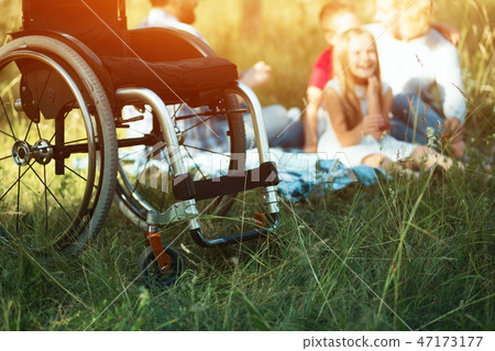 Focus on emply wheelchair on the foreground while happy family rest on the background 47173177