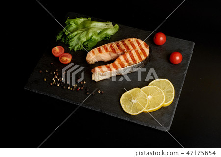 Grilled trout steak with a lemon and salad on a slate plate. 47175654