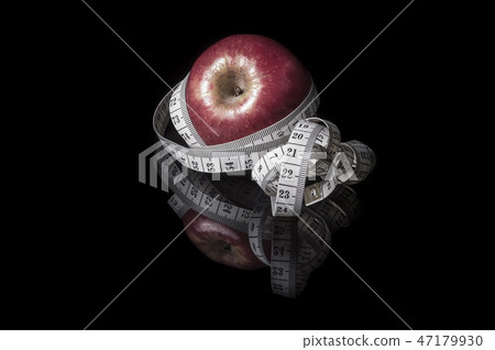 apple surrounded with measurement tape on blac 47179930