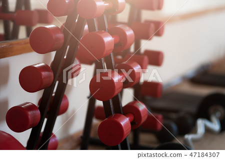 Rows of red metal dumbbells on rack in the gym 47184307