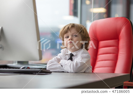 Little businessman is sitting at the office table and using a computer. 47186005