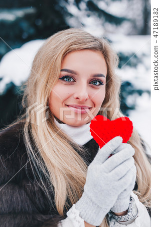 Portrait of a beautifull smiling woman in winter forest holding red Valentine's heart in the hands. 47189182