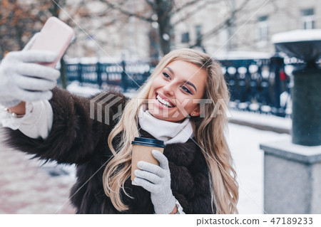 Beautiful girl with takes funny winter selfie on city street 47189233