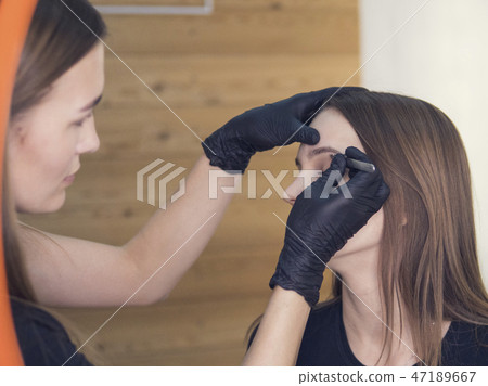 Artistic correction of eyebrows of a young girl. professional make-up in the beauty salon master 47189667