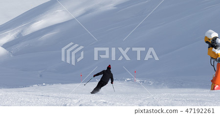 Skier downhill on snowy ski slope with snow cannon 47192261
