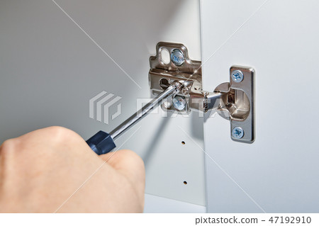 Handyman adjusts hinges on door of office table Handyman adjusts hinges on door of office table 47192910