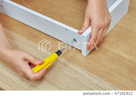 Handyman tightens screw into wooden drawer. 47192922